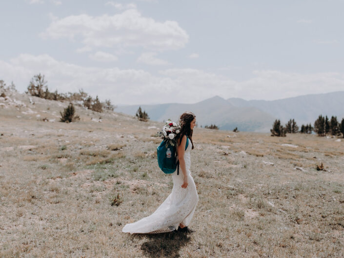 bride walking across mountain tundra with backpack