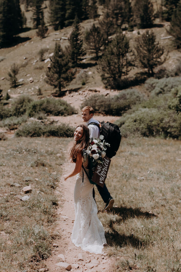 bride and groom walking and laughing with just married sign on backpack