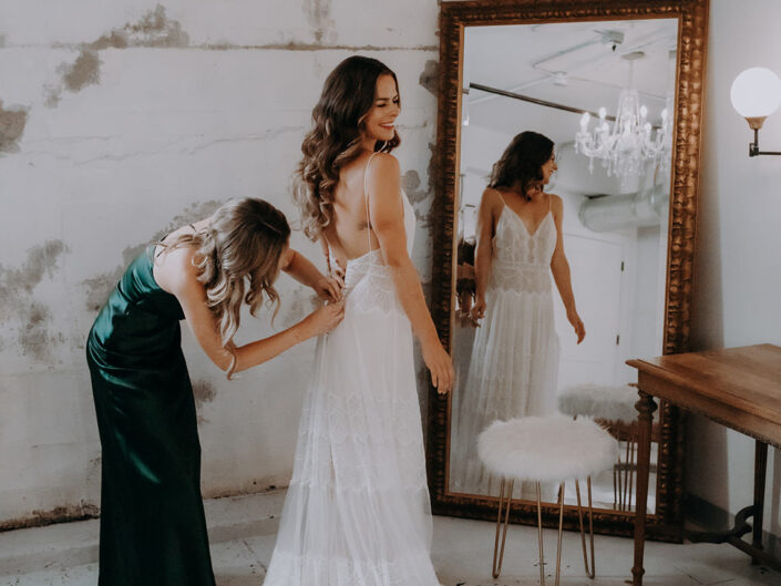brides sister buttons up her dress in front of mirror