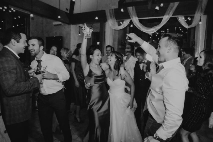 bride and maid of honor dance together in a crowd during reception party