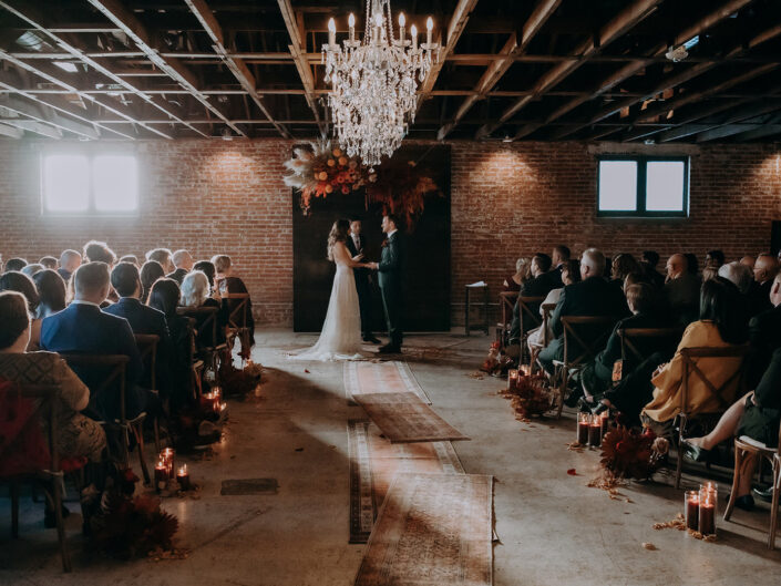 wide shot of indoor ceremony with brick walls and chandeliers