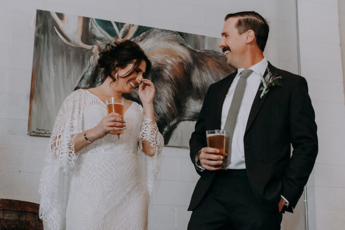 bride and groom laugh and cheers beer